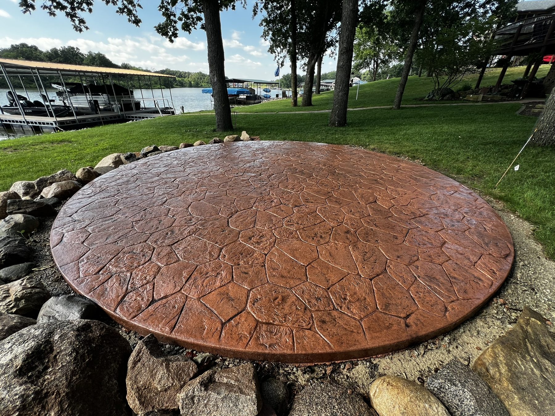 Round stamped concrete patio with a stone pattern beside a lake