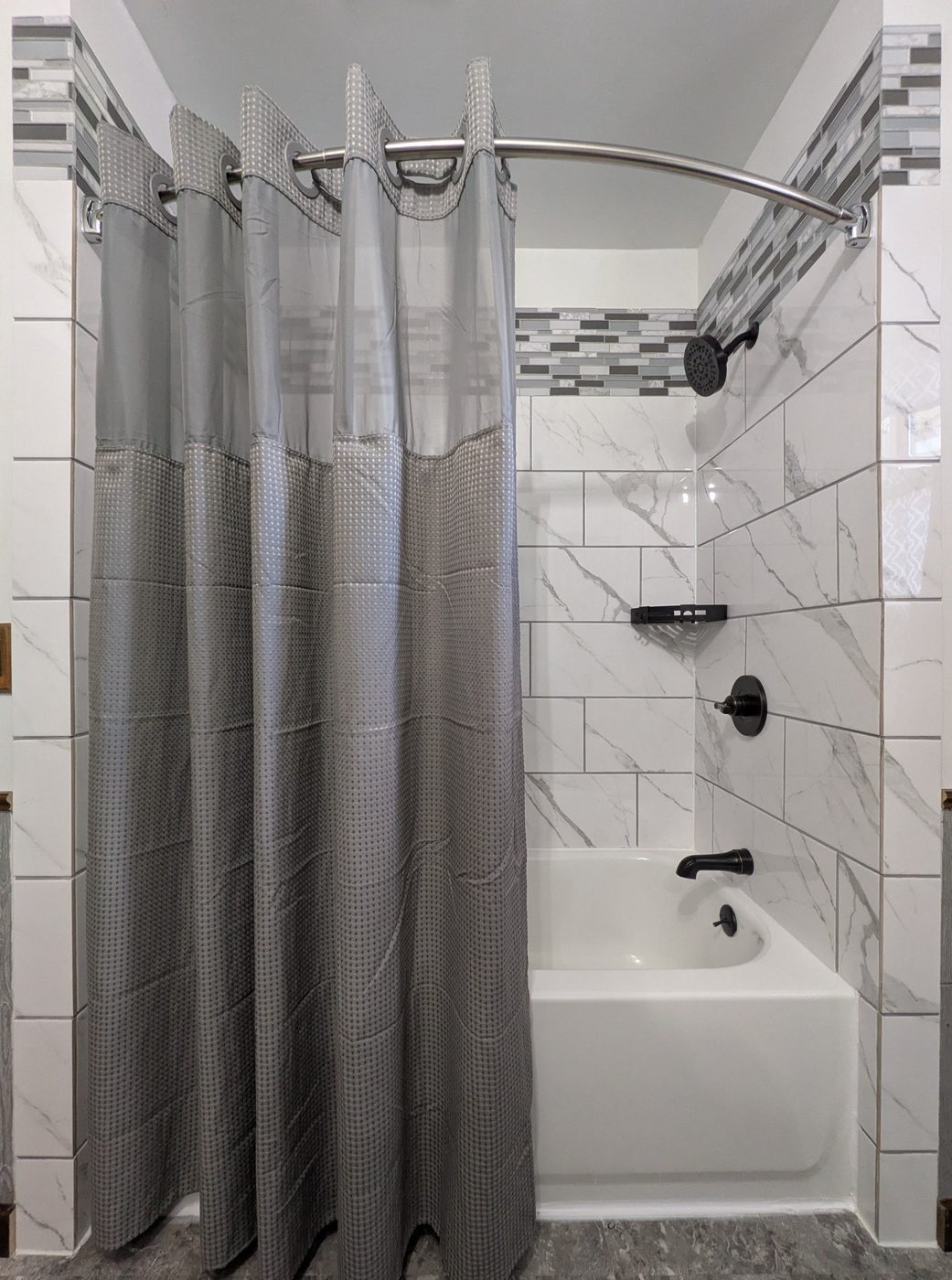Remodeled tub surround with marble-look tile and a glass mosaic accent band